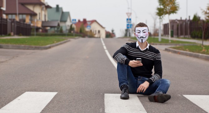 hacker in masked members of Anonymous with mobile phone