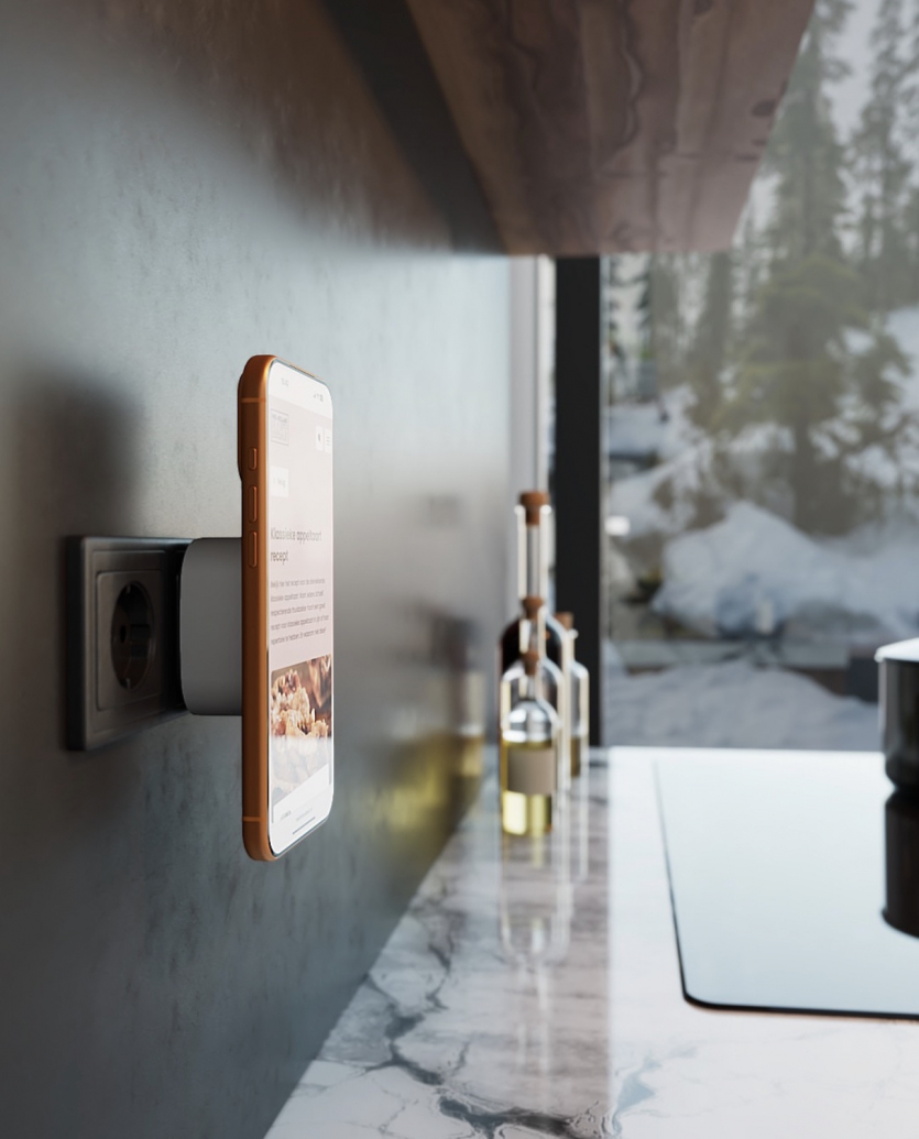 Смартфон із відкритим на екрані рецептом примагнічений до компактного зарядного адаптера Zens Wireless Charging Adapter, що вставлений безпосередньо в чорну розетку на кухонній стіні.