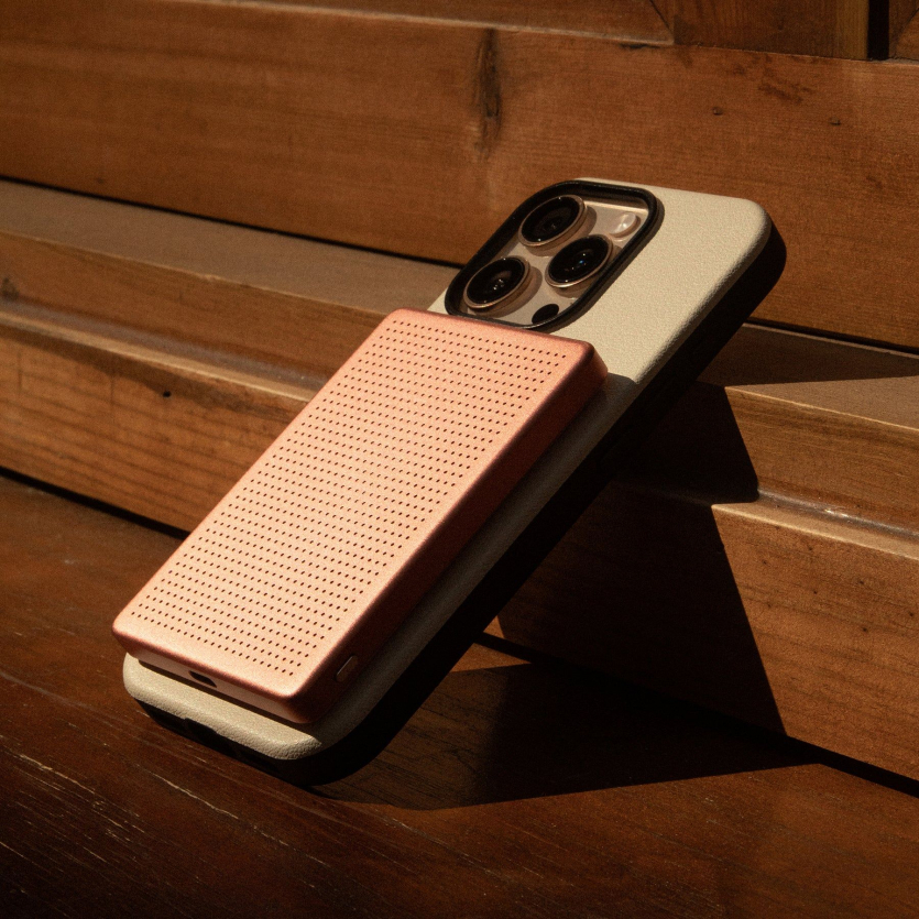 Рожевий магнітний павербанк Native Union Active 5000 mAh, прикріплений до задньої панелі iPhone у світлому чохлі на дерев'яній поверхні.