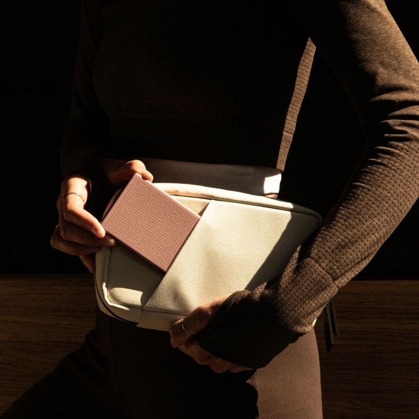 Людина кладе ультратонкий павербанк Native Union Active 5000 mAh у зовнішню кишеню світлої поясної сумки.