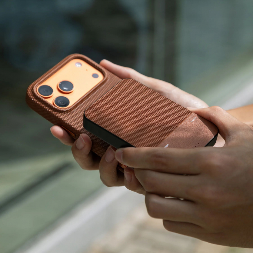 Коричневий магнітний павербанк Native Union (Re)Classic 10000 mAh, прикріплений до iPhone, на розмитому фоні природи.