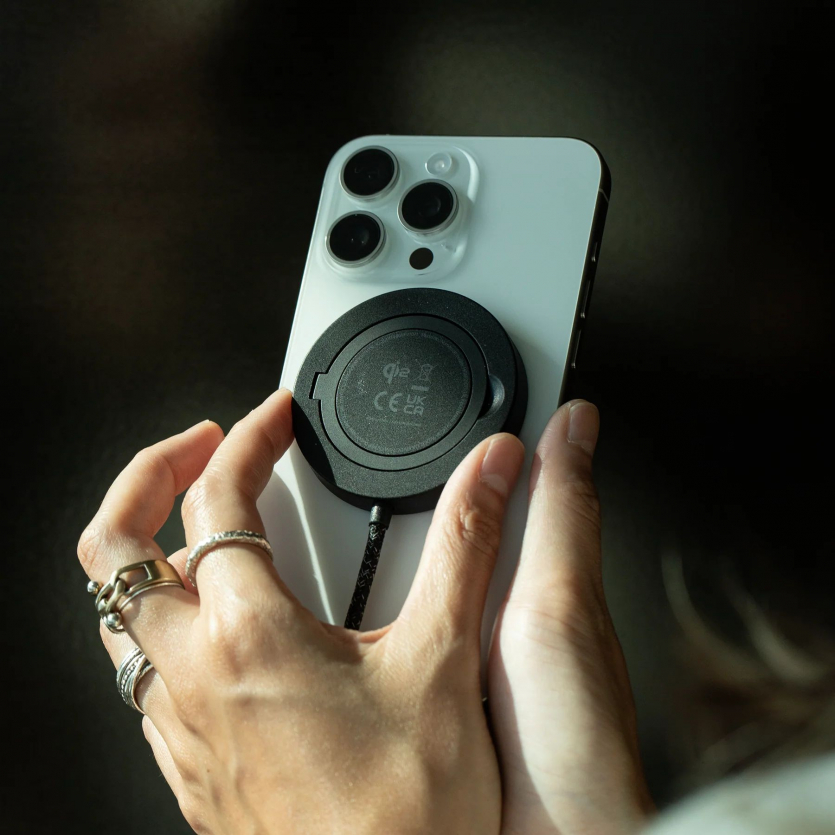 Процес кріплення чорної магнітної зарядки Native Union SnapStand із вбудованою підставкою до задньої панелі білого iPhone.