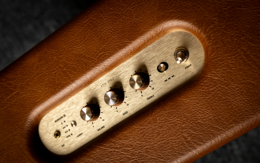 Макрофото золотої латунної панелі керування акустикою Marshall Woburn III з аналоговими регуляторами гучності, баса та високих частот і механічним тумблером.