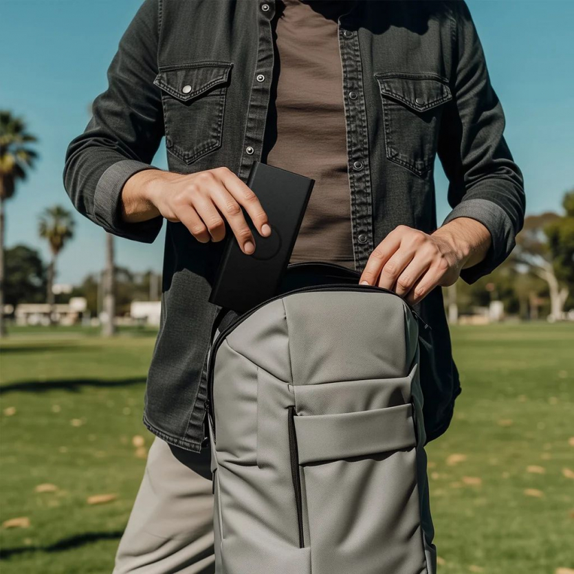 Користувач кладе чорний футляр для окулярів Satechi Vegan Leather FindAll у міський рюкзак під час прогулянки парком.